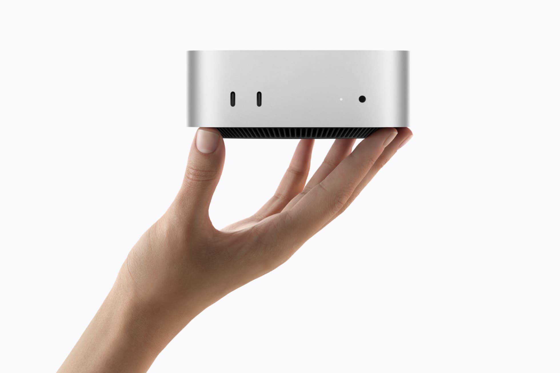 Hand holding the silver Mac mini, showing front USB-C ports, status light, and headphone jack