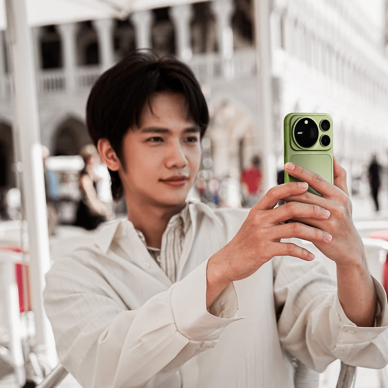Man at a Venice café table photographing with a Moss Green Honor Magic 9 Pro Max, its ARRI-branded camera island facing the viewer