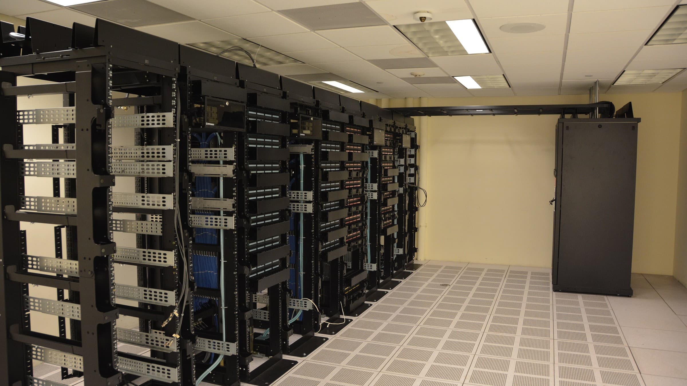 Rows of black server racks and a standalone cabinet in a data centre with a raised perforated floor